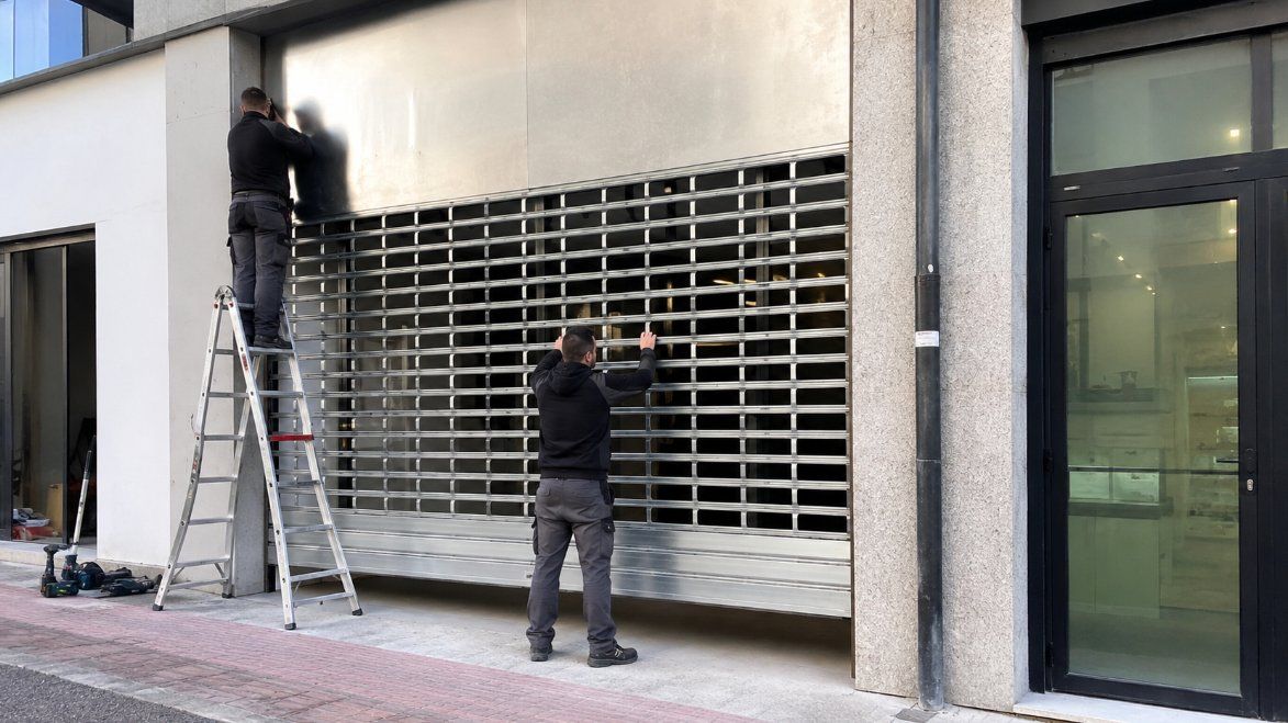 Técnicos instalando una persiana metálica de seguridad en un comercio